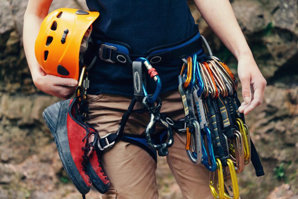 Nachhaltig reisen und Klettern - Stehende Frau mit Kletterausrüstung und Helm im Freien, Vorderansicht.