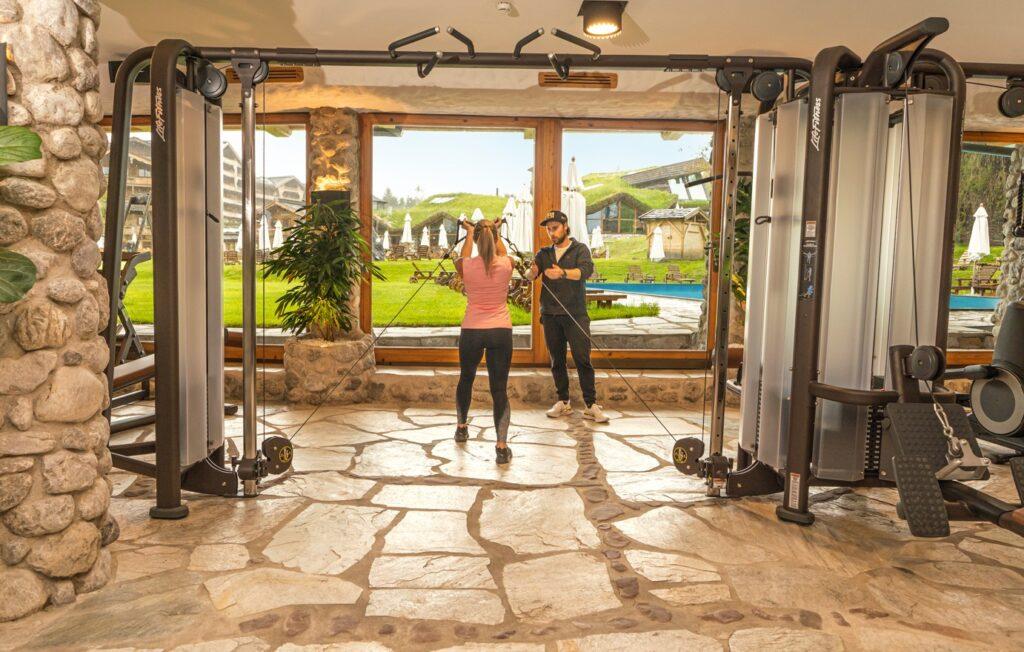 Personal Trainer mit Frau an der Zugmaschine im Fitnessraum vom Stanglwirt