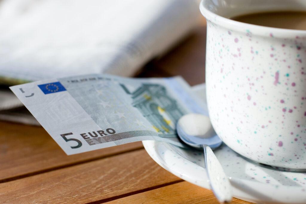 fünf Euroschein an einer Kaffeetasse – Trinkgeld geben auf Reisen