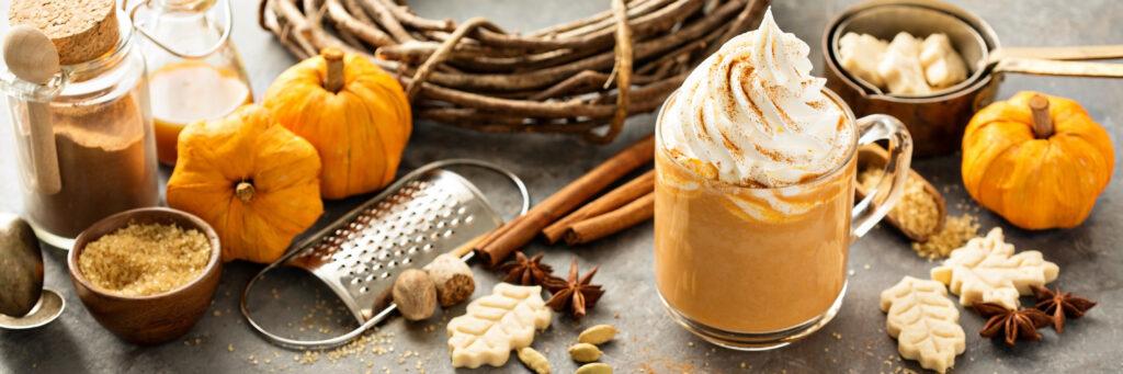 Pumpkin spice latte in a glass mug with cinnamon, nutmeg and cookies
