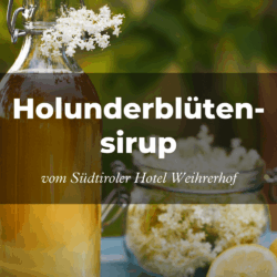 Glasflasche und Glas mit Holunderblütensirup, garniert mit Holunderblüten und einer Zitronenscheibe, vor einem unscharfen grünen Hintergrund. Text: „Holunderblütensirup aus dem Südtiroler Hotel Weihrerhof.“