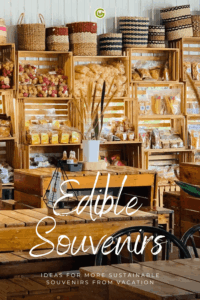 Shelves made of light-colored wood are filled with food items in transparent packaging. Smaller packages and jars can be seen on the lower shelves. The text “Edible Souvenirs” is superimposed across the image in white, handwritten lettering, with the text “Ideas for more sustainable vacation souvenirs” appearing below it in smaller font.