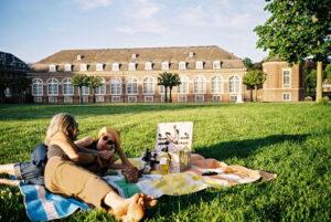 Zwei Personen liegen auf einer Picknickdecke auf einer Wiese vor dem Schloss Nordkirchen im Münsterland
