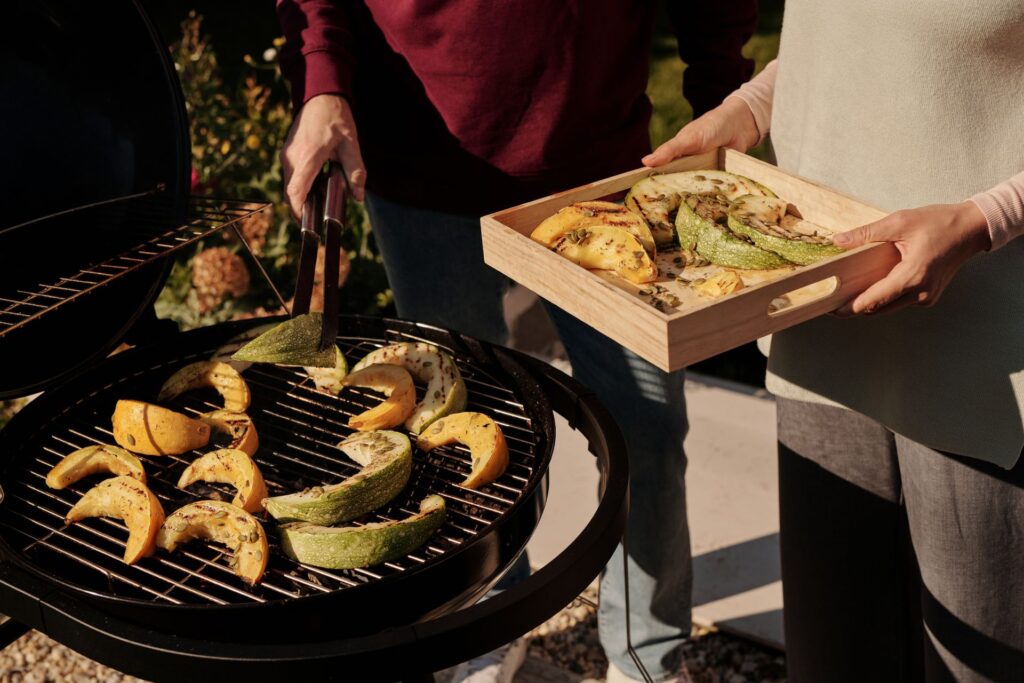 Grill mit Grillgemüse und Frauenhände halten ein Holztablett