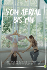 Frau hängt kopfüber in einem Aerial-Yoga-Tuch, während eine andere Frau sie anleitet, im hellen Raum mit großen Fenstern und grüner Außenansicht, Text 'VON AERIAL BIS YIN' und 'YOGA-STILE, DIE DU KENNEN SOLLTEST – UND WO DU SIE IM URLAUB ERLERNEN KANNST'