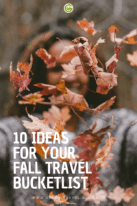 In the foreground, autumnal brown and orange maple leaves are floating in the air. Behind them stands a person with long hair. The background is blurred and features autumnal colors. At the bottom of the image, in large white capital letters, it reads: “10 IDEAS FOR YOUR FALL TRAVEL BUCKET LIST.”