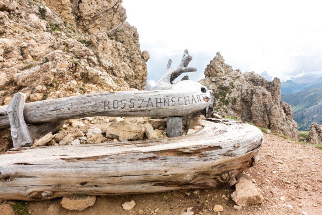 Bank mit der Aufschrift Rosszahnscharte am Gipfel vom Wanderweg in den Dolomiten