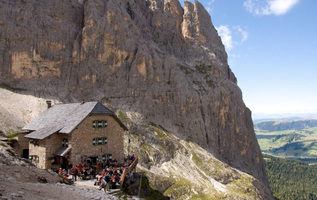Langkofelhütte in den Dolomiten mit Blick auf den Berg und die Landschaft im Sommer. Vor der Hütte sind Menschen