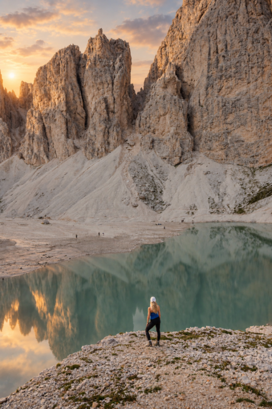 Marnie Spögler steht in den Dolomiten an einem See. Die Felsen spiegeln sich im Wasser.