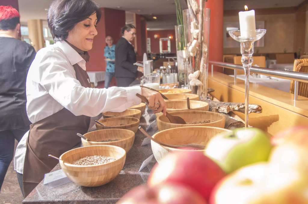 Mitarbeiterin steht am Zero Waste Frühstücksbuffet mit Glas und Holzschüsseln